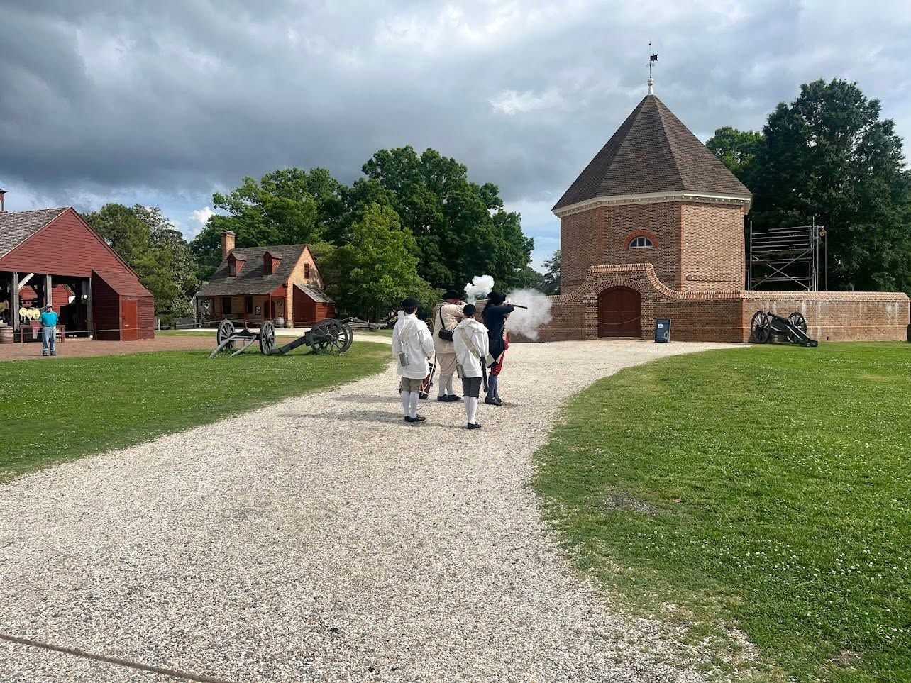 People walking on a gravel path toward historic stone buildings under a cloudy sky.