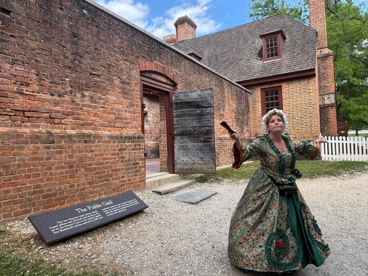 Woman in green dress standing by a historic brick building and sign in a gravel courtyard