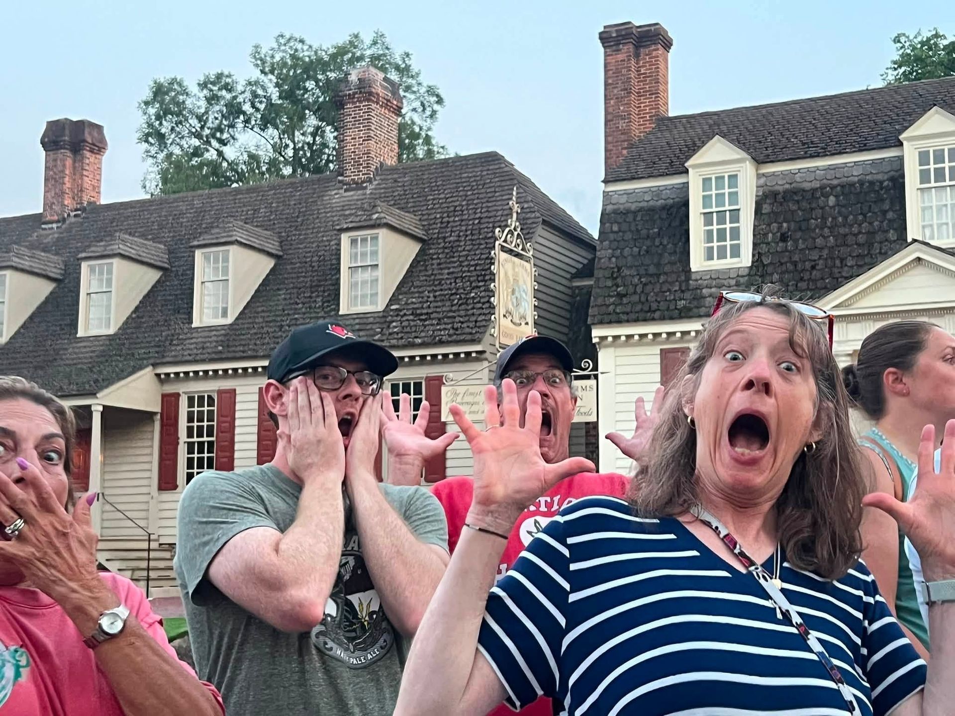 People outdoors in front of historic houses, reacting with surprised expressions and raised hands