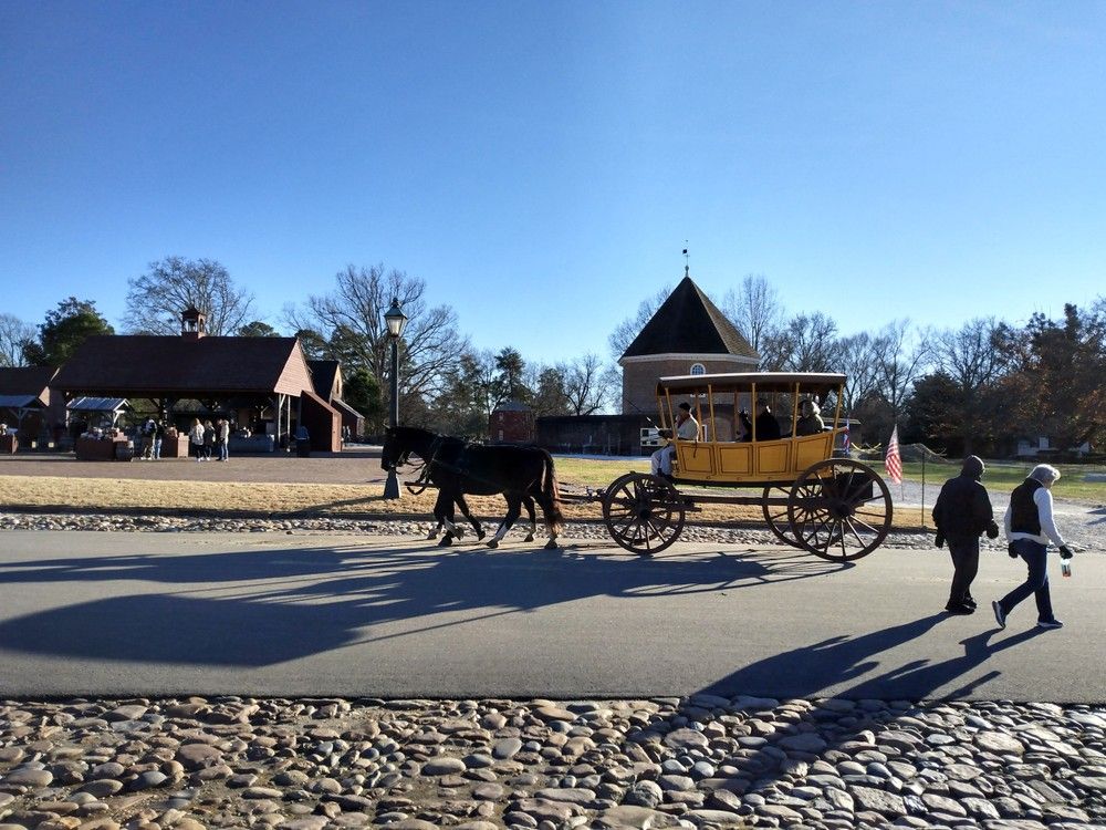 Horse-drawn carriage on a paved road in a historical village; two pedestrians walk by.