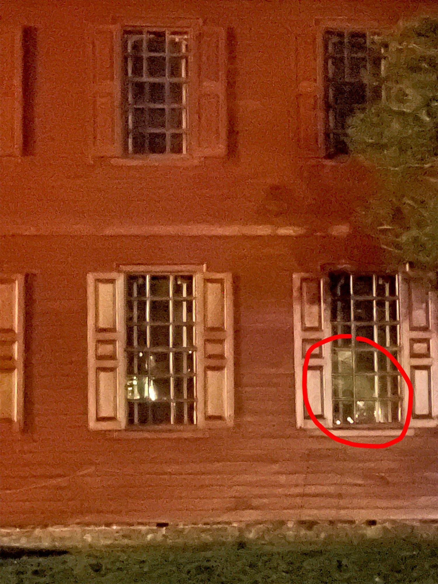 Red brick building with barred windows, one window circled, possibly showing a reflection.