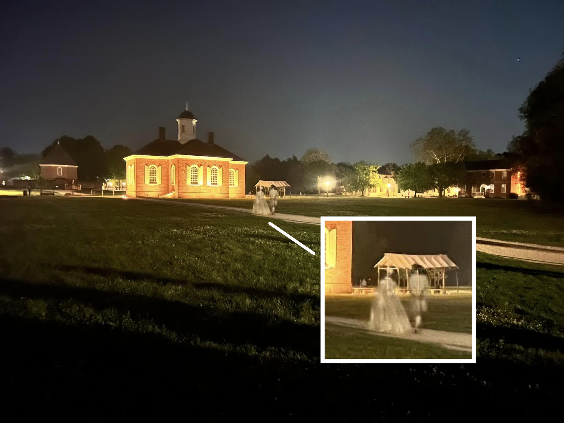 Night photo of a historic brick building with lights. A ghostly couple walks toward a gazebo on the grass.