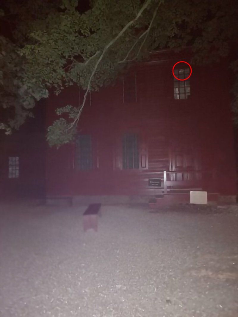 Red-colored building at night. A round object is circled in red on the upper right window.