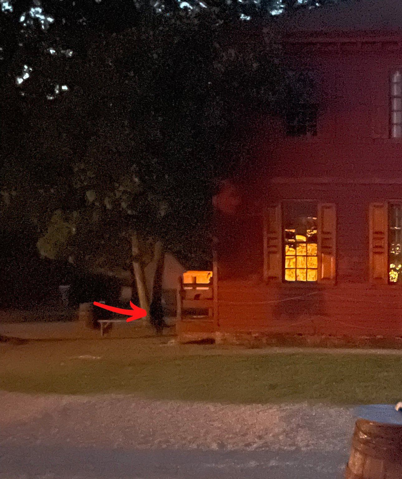 A building with lit windows at night, a dark figure and a gate.