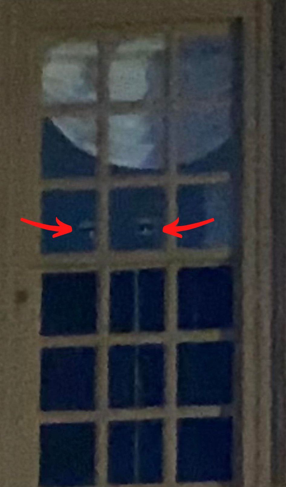 Window with two glowing eyes visible in the dark interior. A moon is reflected in the glass.
