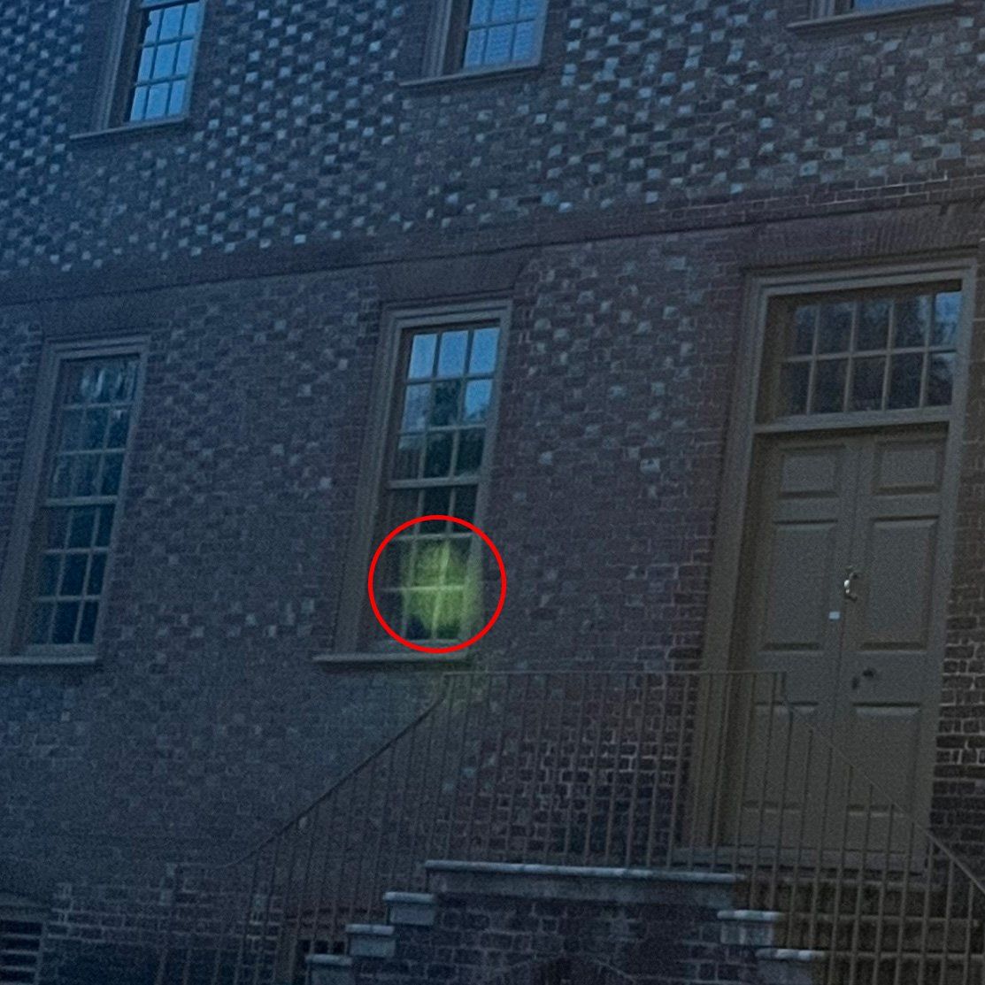 A building with a brick facade at night. A red circle highlights a glowing green shape in a window.
