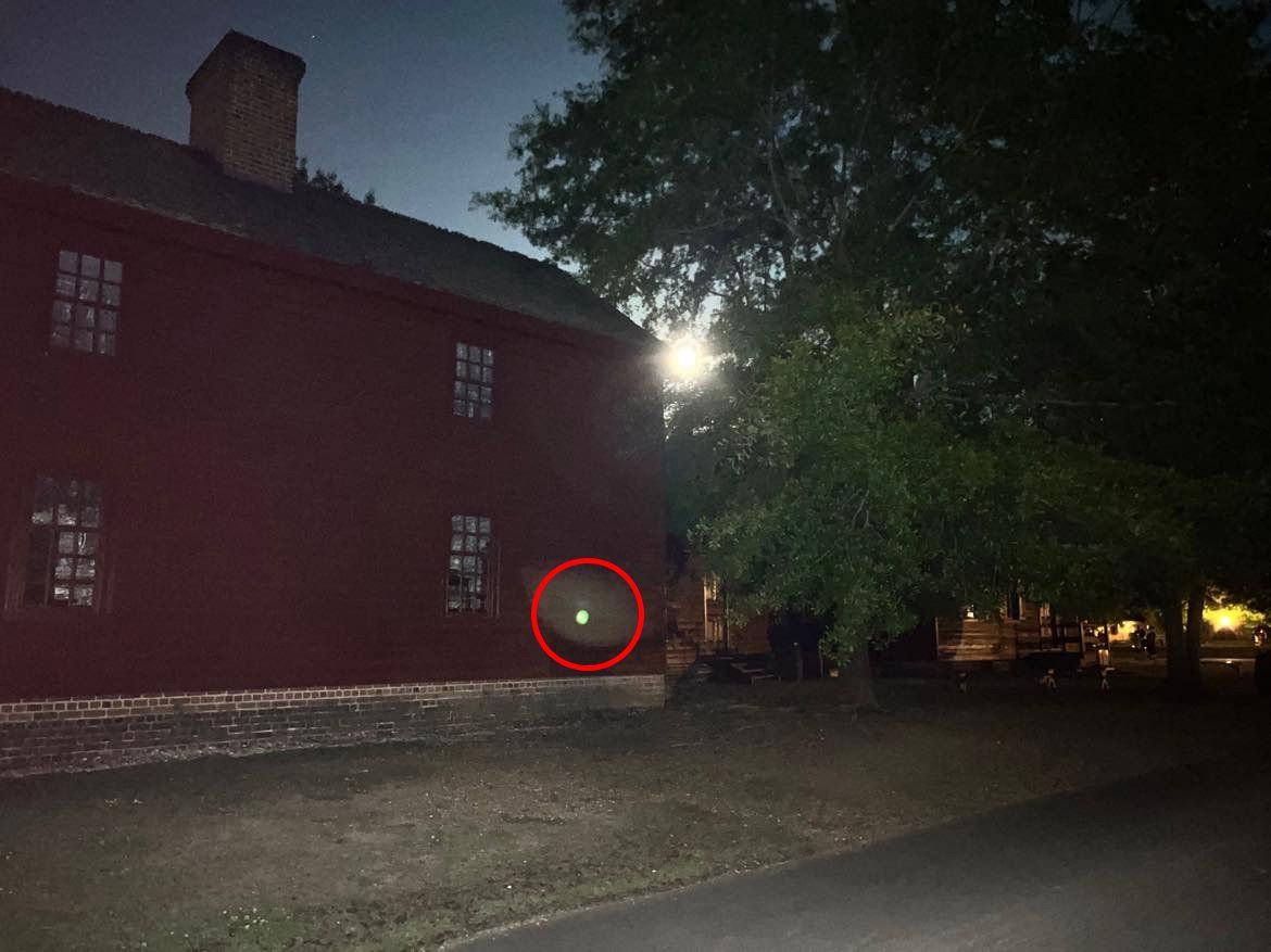 Red-painted building at night with a bright, round, glowing light circled in red.