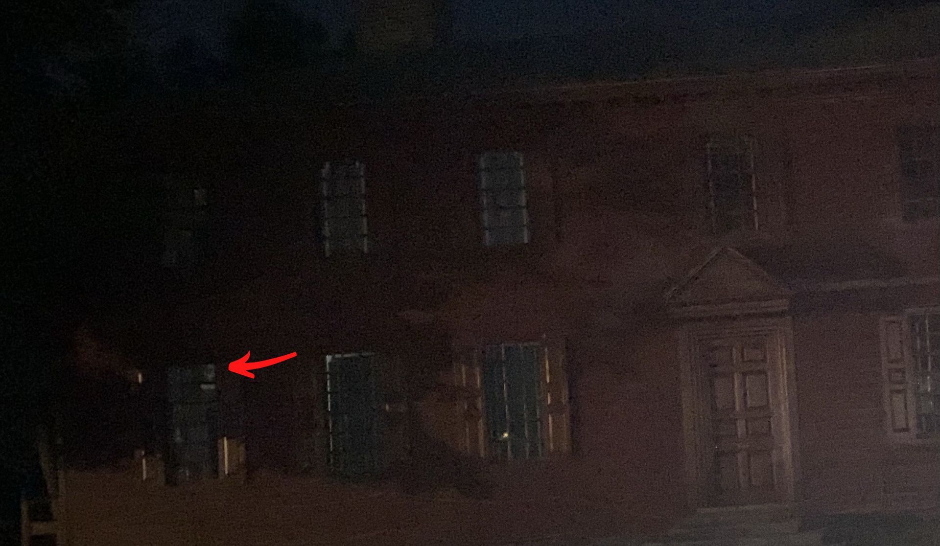 Dark brick house exterior at night. Arrow points to a window.