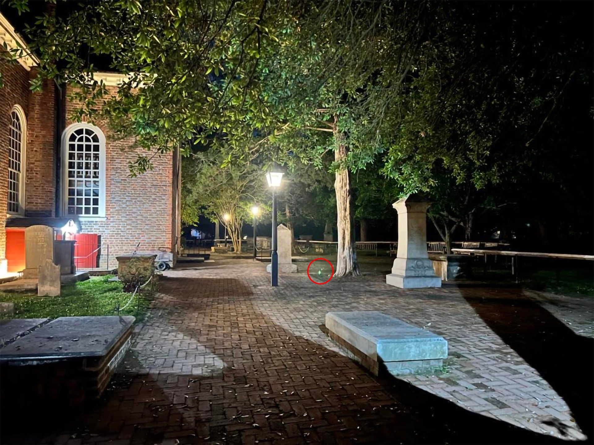 Brick building with arched windows and a walkway, a tree, and tombstones at night.