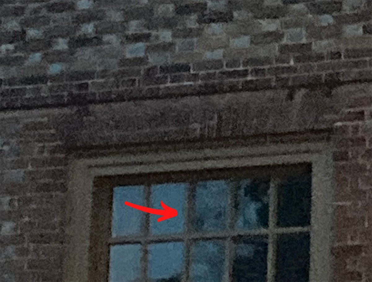 Brick building exterior with window; red arrow pointing to reflection within glass panes.