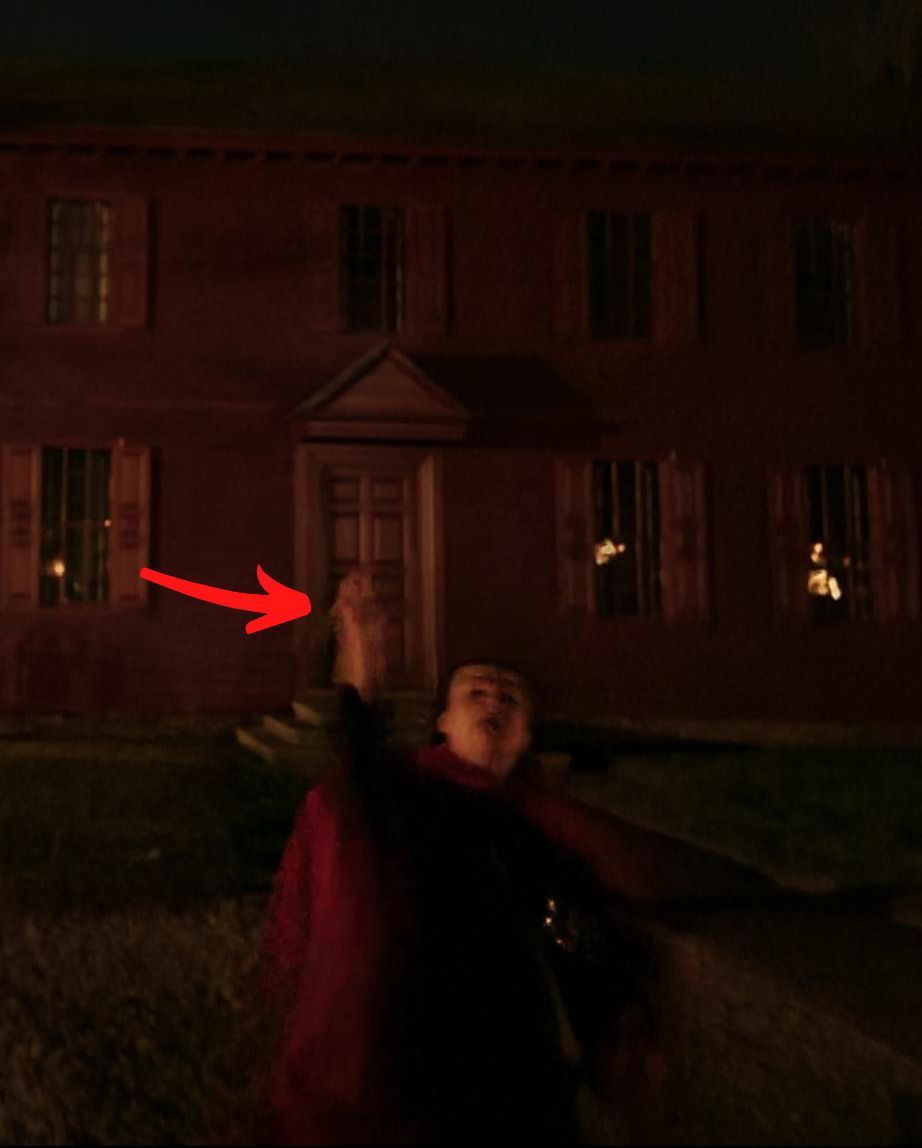 Person in red cape raises hand toward a dark brick building at night.