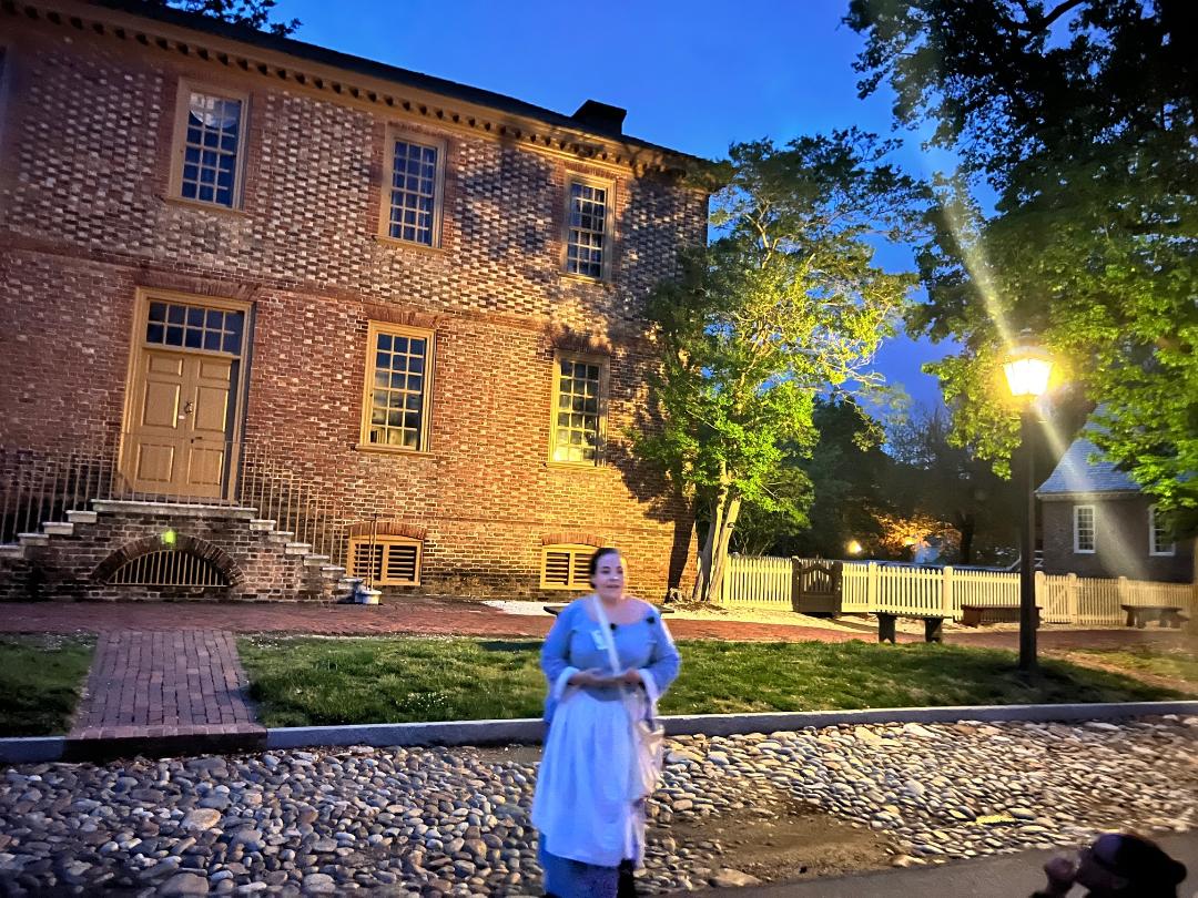 Woman in blue dress stands in front of a brick building at dusk.