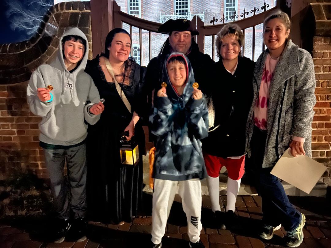 Family poses near a brick building at night; some in historical costumes, holding treats.