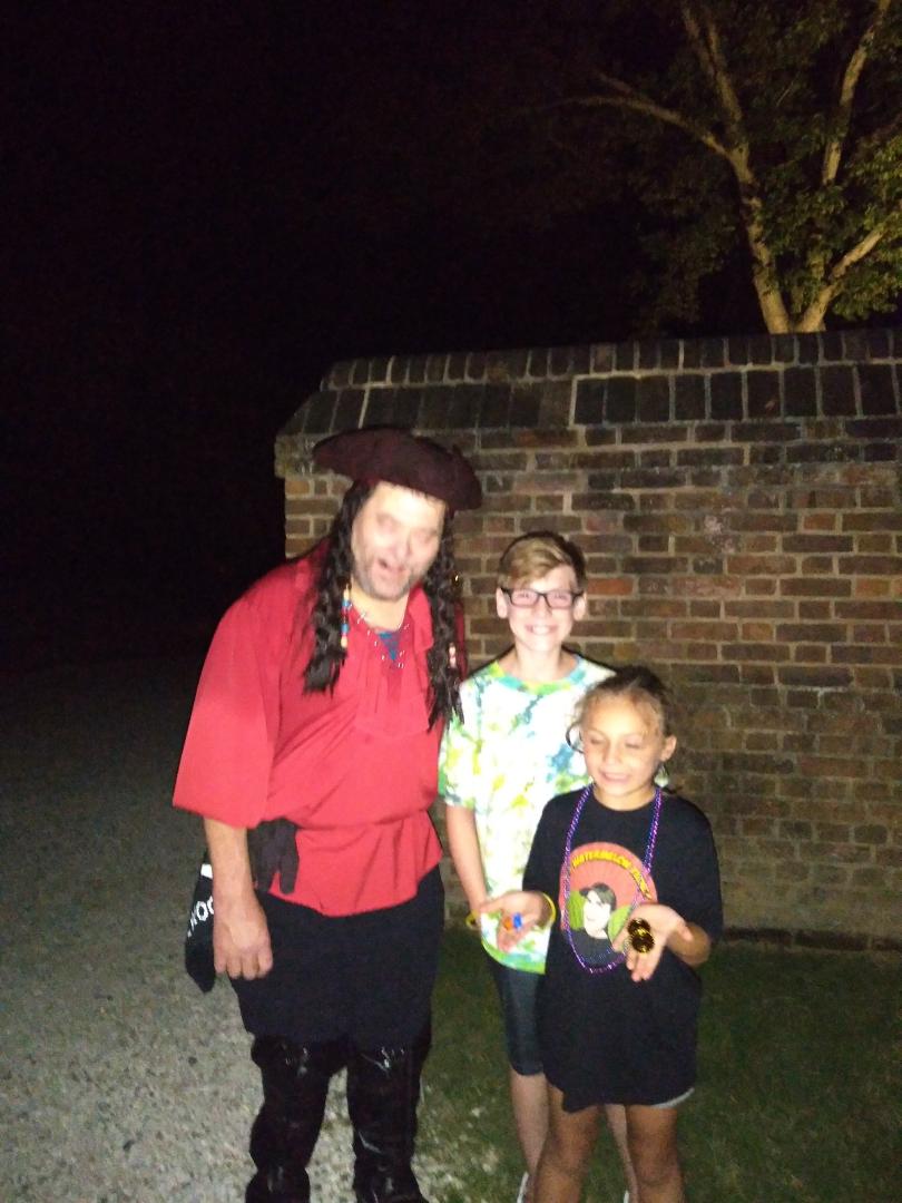 A person in pirate costume stands with two children at night near a brick wall.