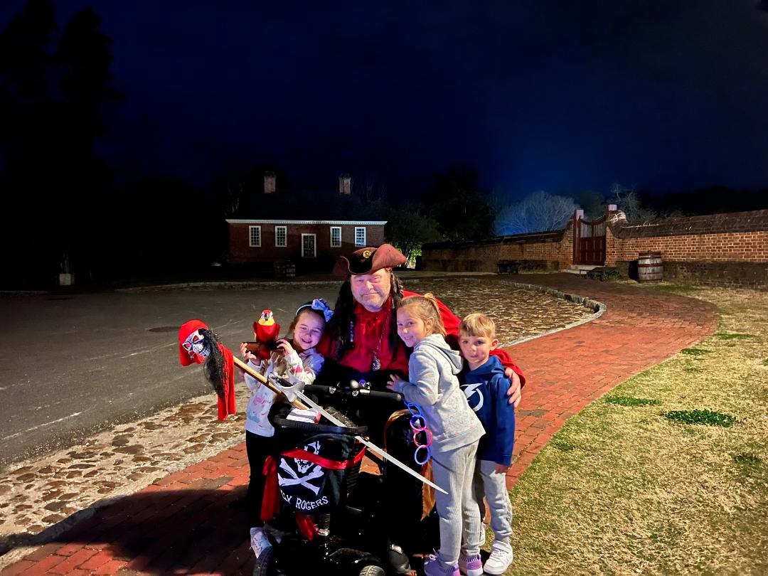 A person dressed as a pirate with three children at night. They stand near a path and building.