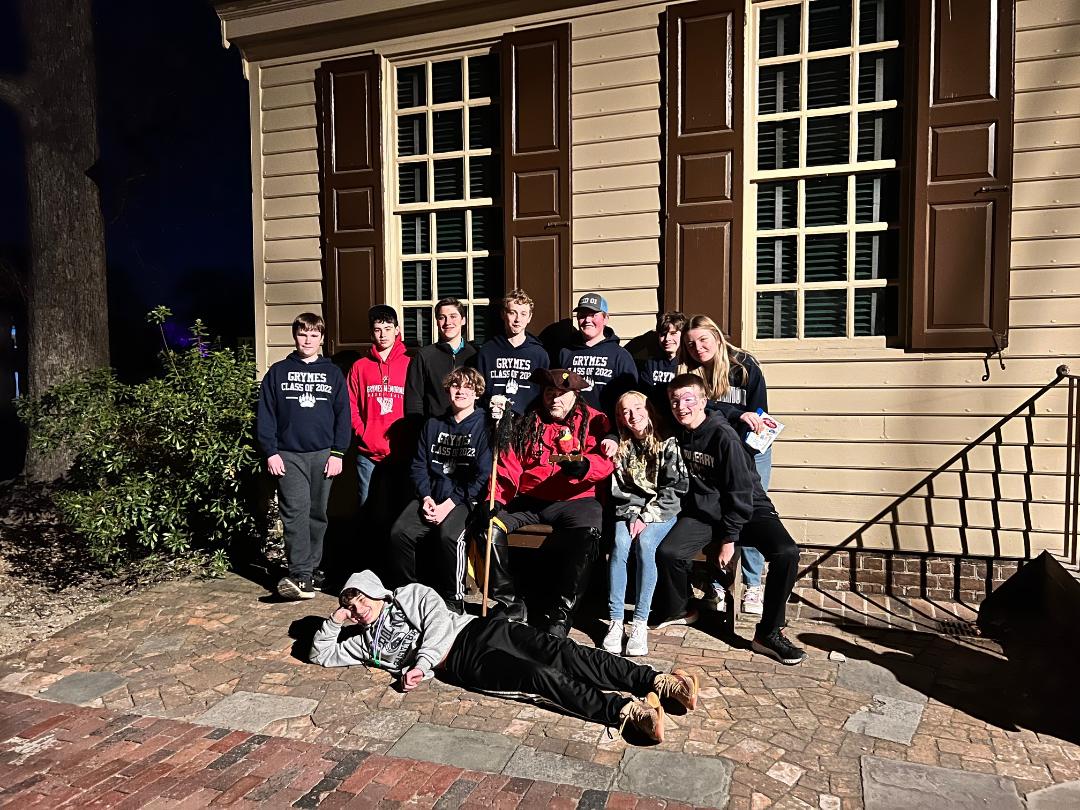 Group of teens pose in front of a building at night. One person lies on the ground.
