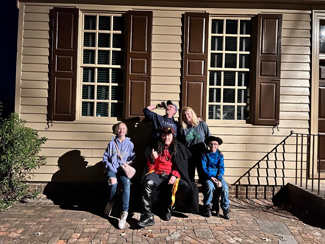 People pose on steps in front of a building with brown shutters. One person is in a red jacket.
