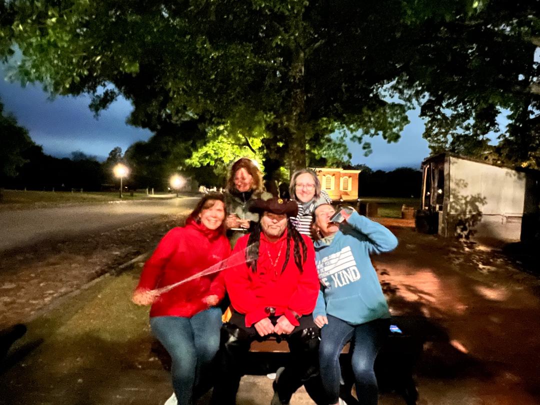 Five people pose outdoors at dusk. Some smile, one points a stick.