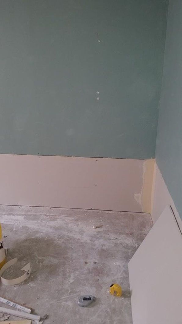 Partially painted empty room with green and pink walls and a bare concrete floor