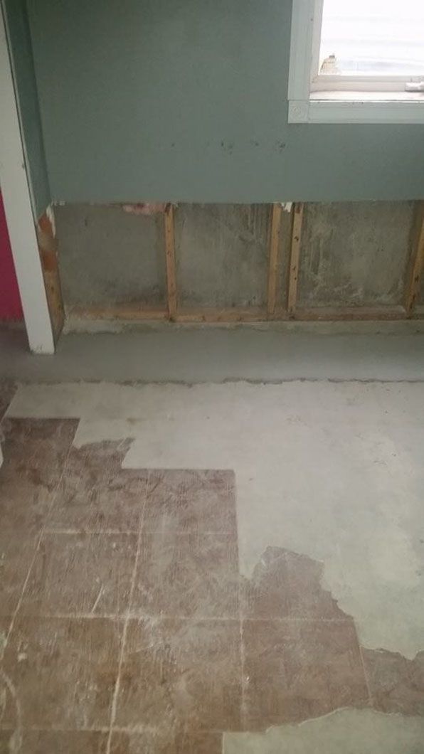 Partially renovated room with exposed wall framing, green walls, and worn flooring patchwork
