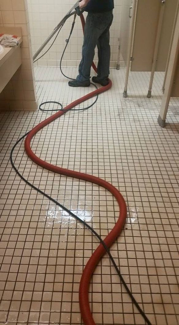 Red hose snaking across tiled floor to a person standing near a wall.