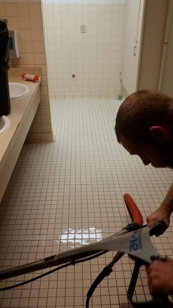 Person using pliers to work on a pipe in a small tiled bathroom