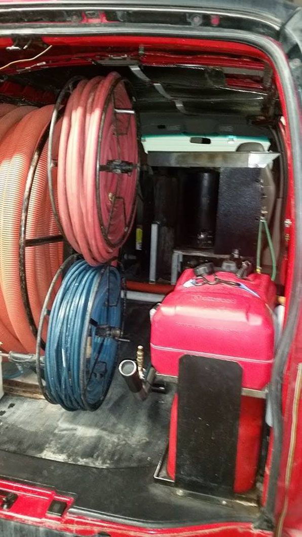 Coiled red and blue hoses and a red tank stored in the back of a vehicle