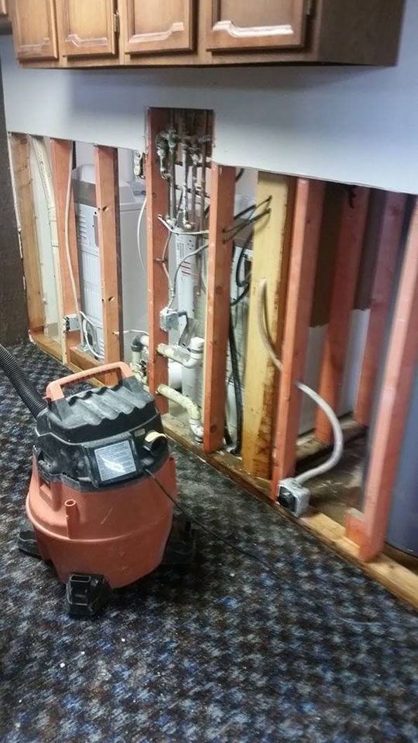 Exposed wall studs and plumbing in a kitchen, with a wet/dry vacuum on patterned carpet.
