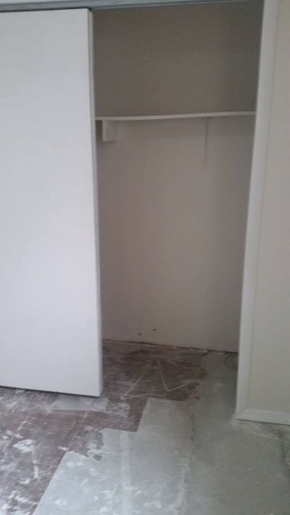 Open closet with sliding white door and empty beige interior, construction debris on the floor.