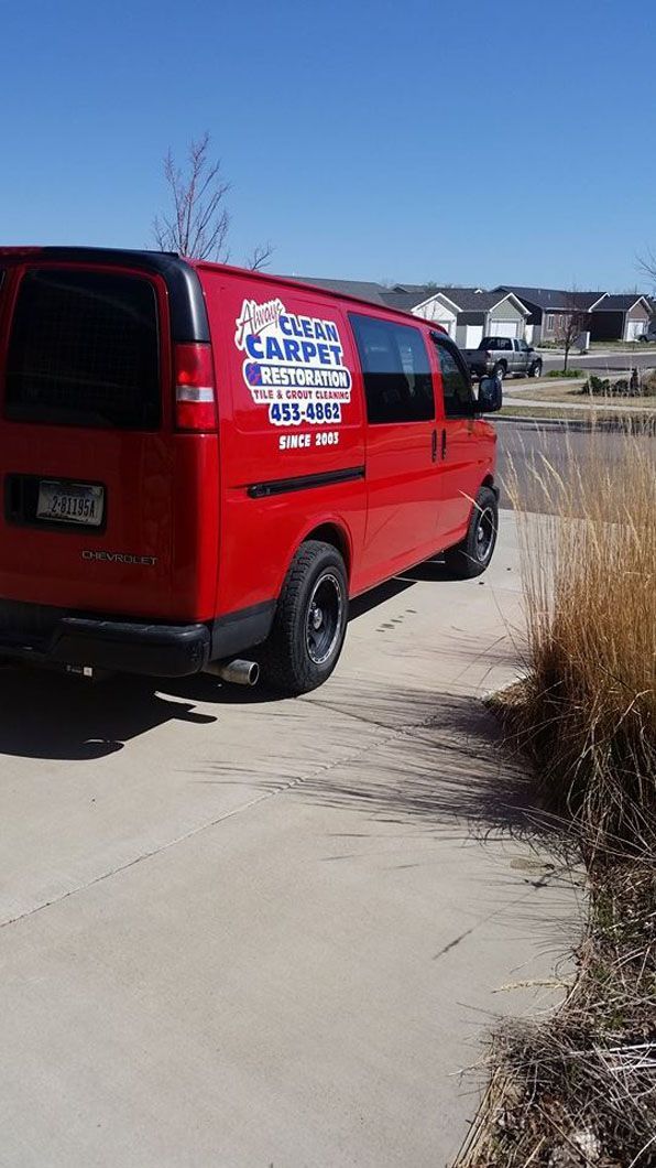 Red van with company logo parked on a driveway beside dry grass under a clear blue sky