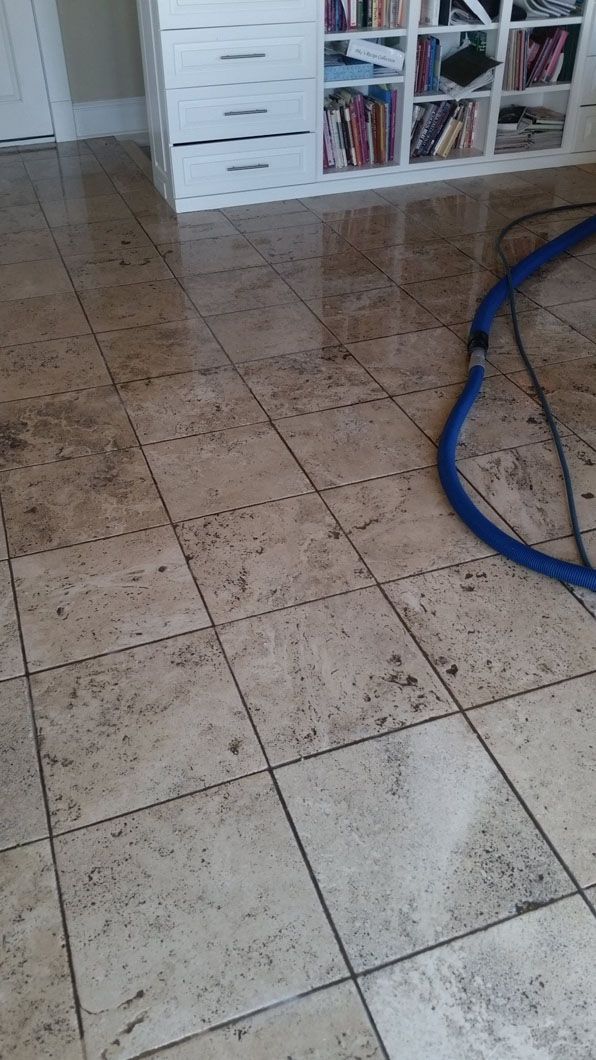 Tiled floor in a room with a blue hose on the right and a white shelving unit in the background