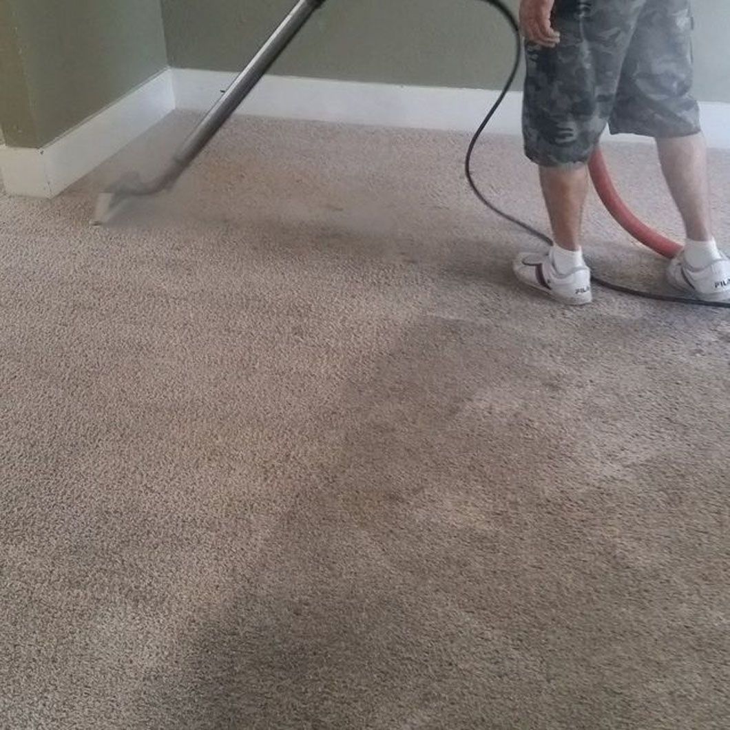 Person vacuuming a beige carpet with a hose in a room.