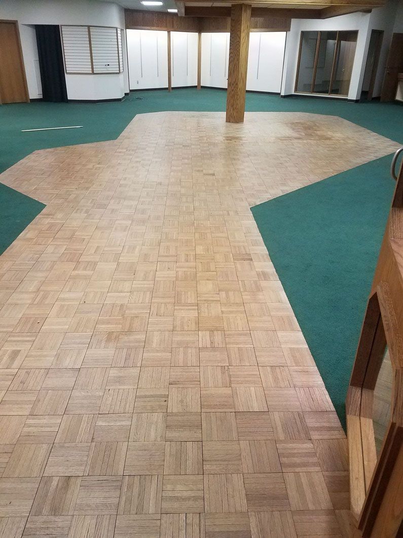 Empty room with green carpet borders and a large parquet wood floor area вокруг wooden pillar