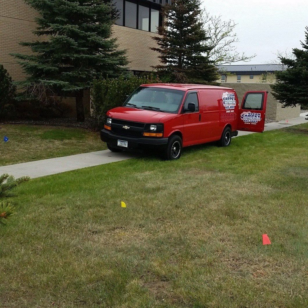 Red delivery van parked on grass beside a sidewalk near a building.