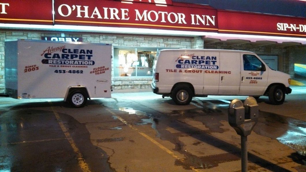 Two white Clean Care vans parked outside O’Haire Motor Inn at night on a wet street.