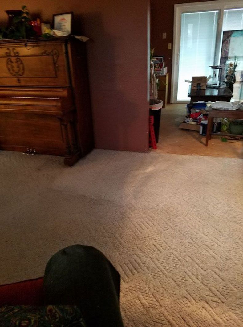 Carpeted living room with upright piano on the left and a dining area visible through a doorway.