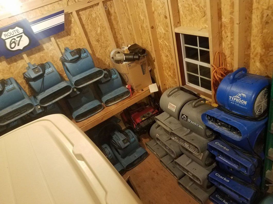 Storage room with stacked blue and gray bags, blue chairs, and a Route 67 sign on the wall