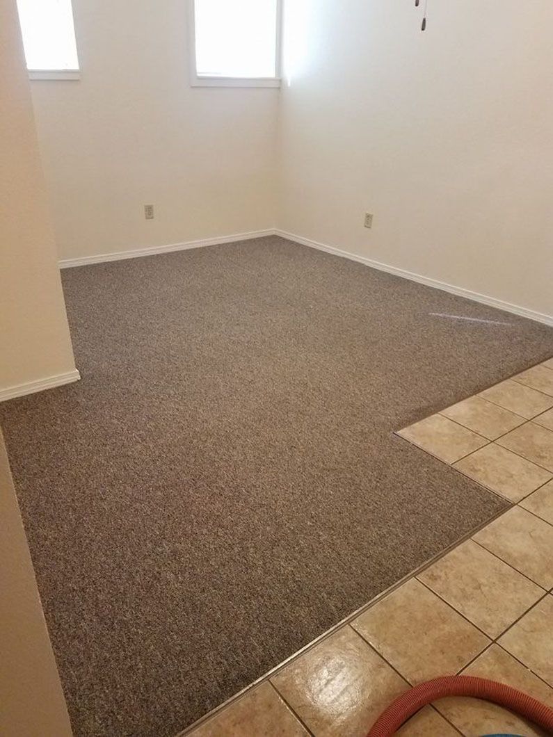 Empty carpeted room with a window, beige walls, and a tile edge in the foreground