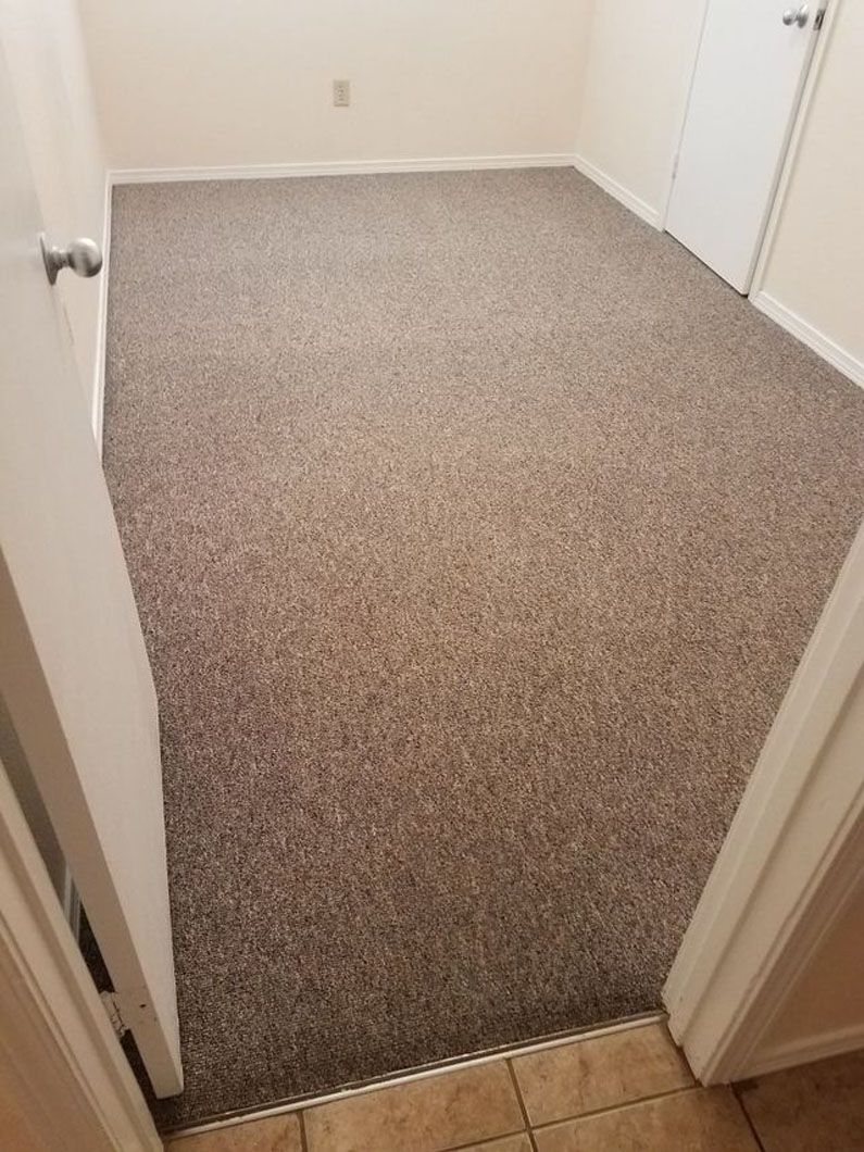 Empty carpeted room with beige walls and white doors, viewed from the doorway.