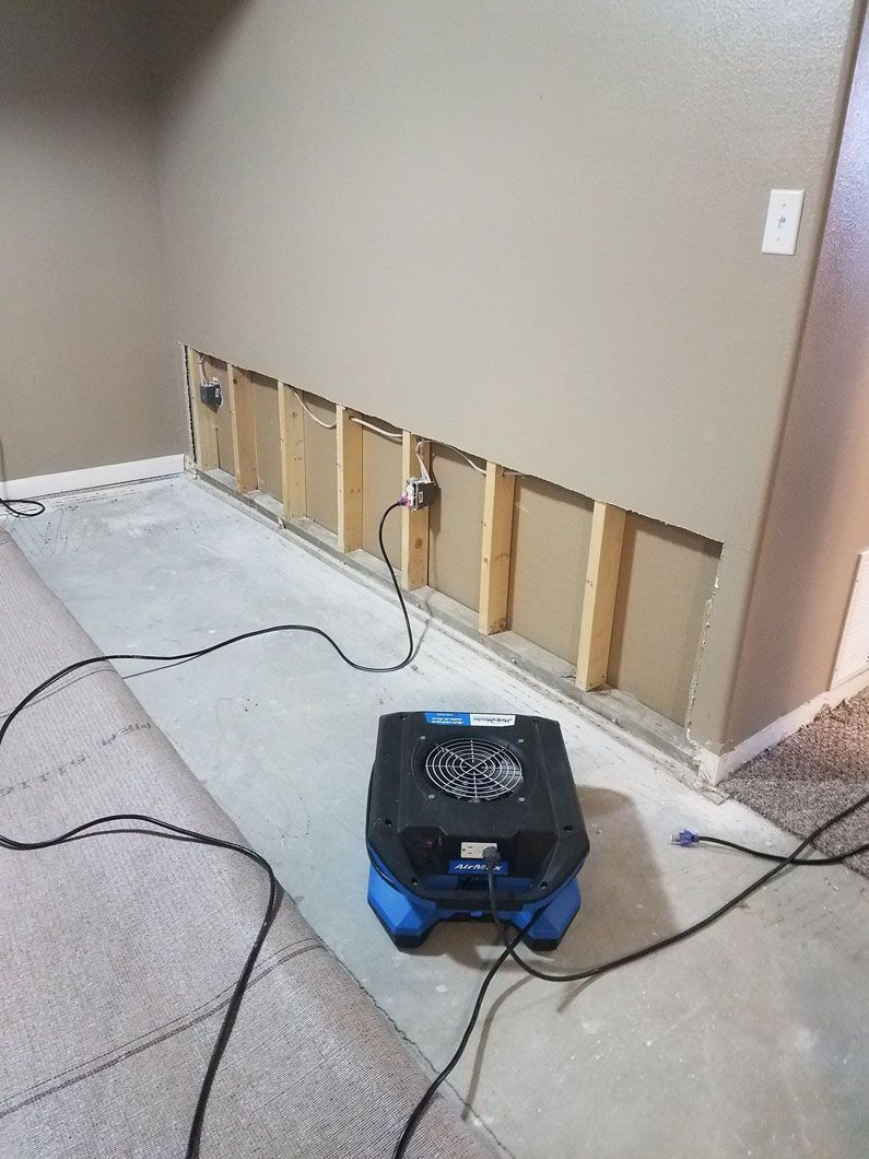 Damaged wall with exposed studs and wiring; black blower on blue base in a room under repair.