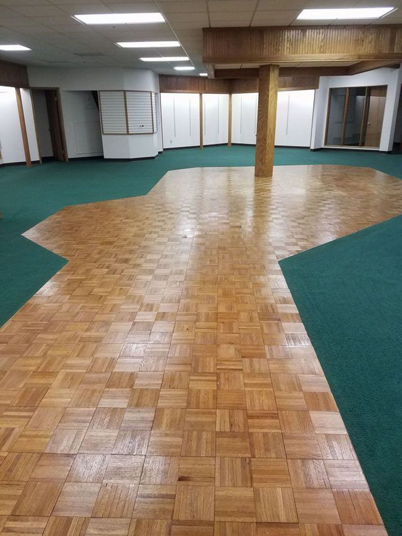 Empty hall with wood parquet floor and green carpet, fluorescent lights, and wood-paneled ceiling.