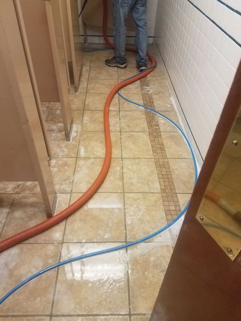 Hallway floor with orange and blue hoses crossing a tiled walkway near a person’s legs