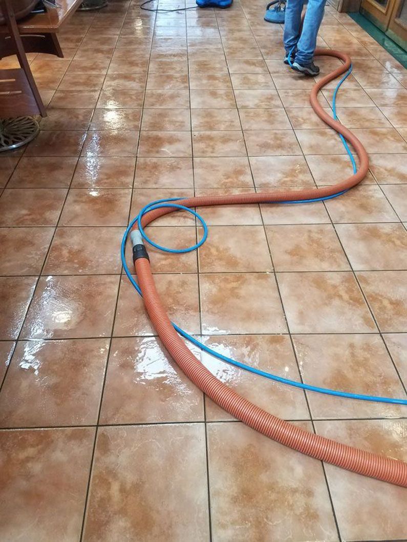 Red and blue hoses snaking across a wet tiled floor, with a worker’s legs visible.