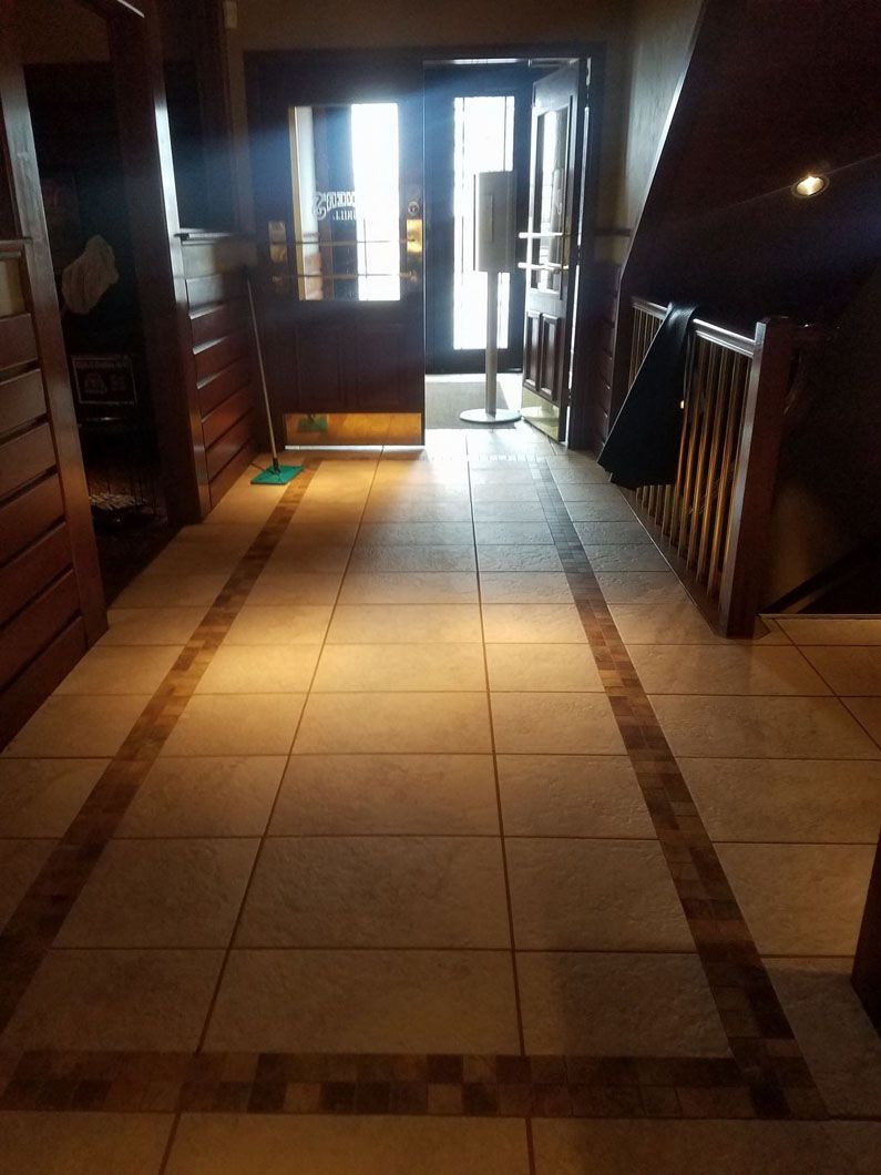Dimly lit tiled hallway with sunlight at the far end and stair railings on both sides