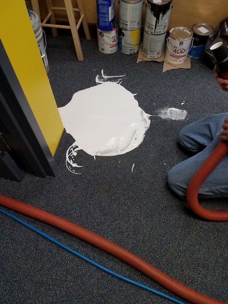 Spilled white liquid on a dark carpet near paint cans and hoses in a workshop