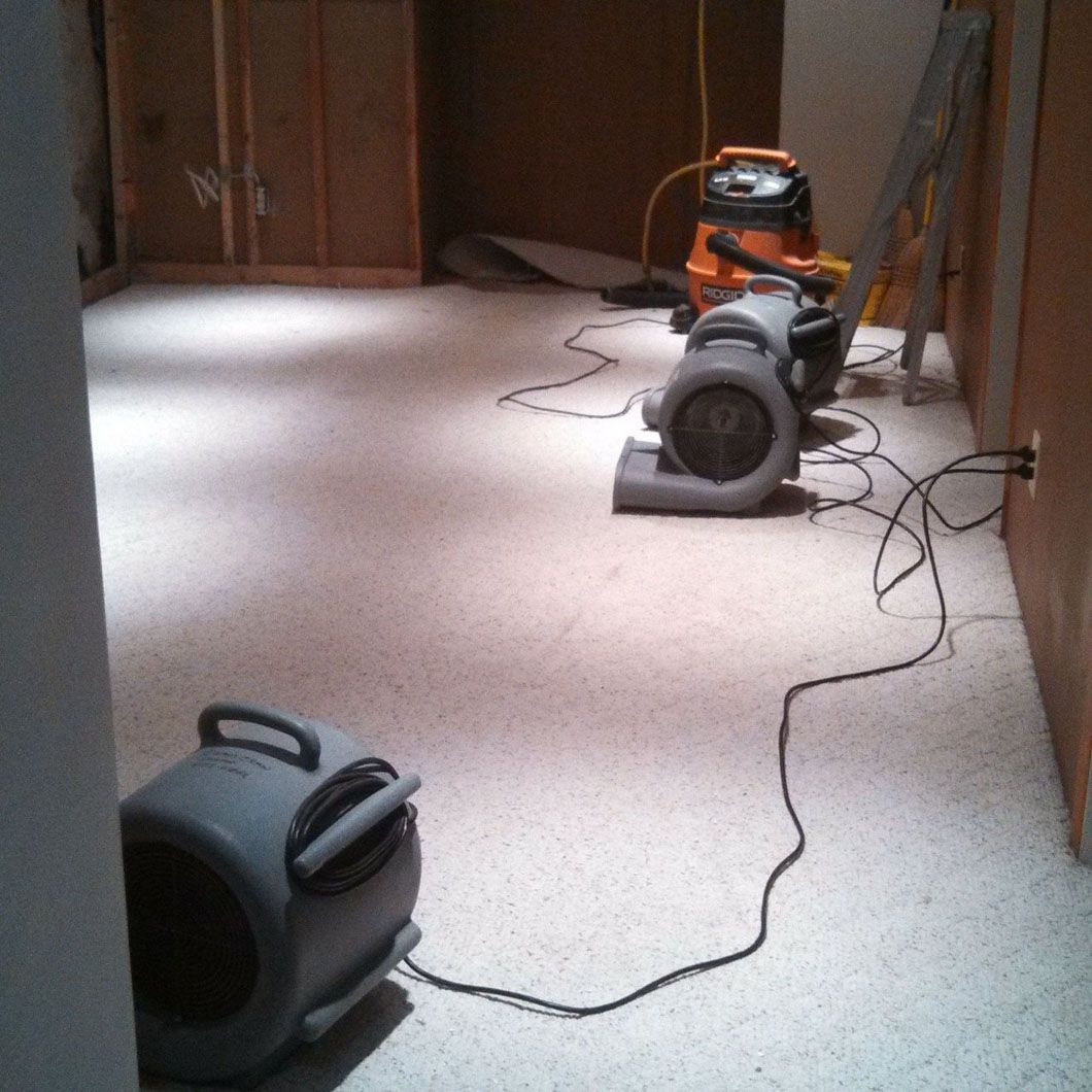 Two vacuum cleaners on a carpeted hallway floor, with cords stretched across the room.
