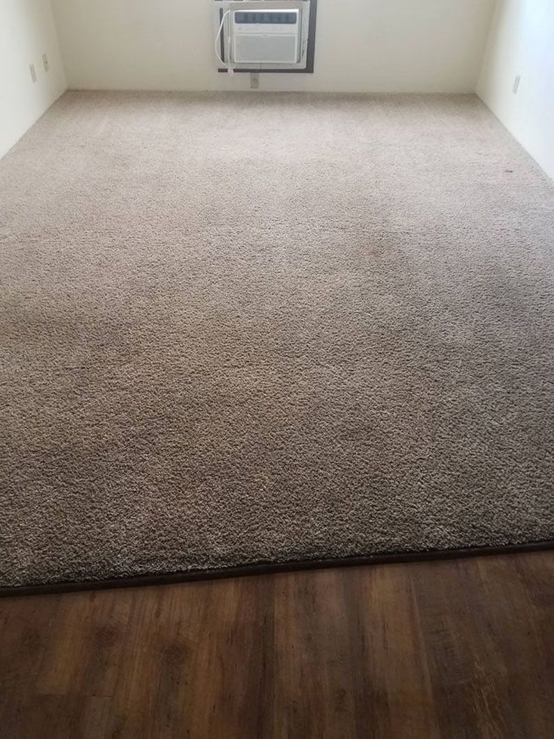Empty carpeted room with a wall-mounted heater and wood flooring in the foreground