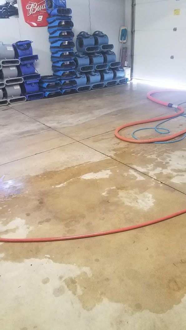 Indoor wet concrete floor with puddles, red hose, and stacked blue equipment in a workshop/garage corner