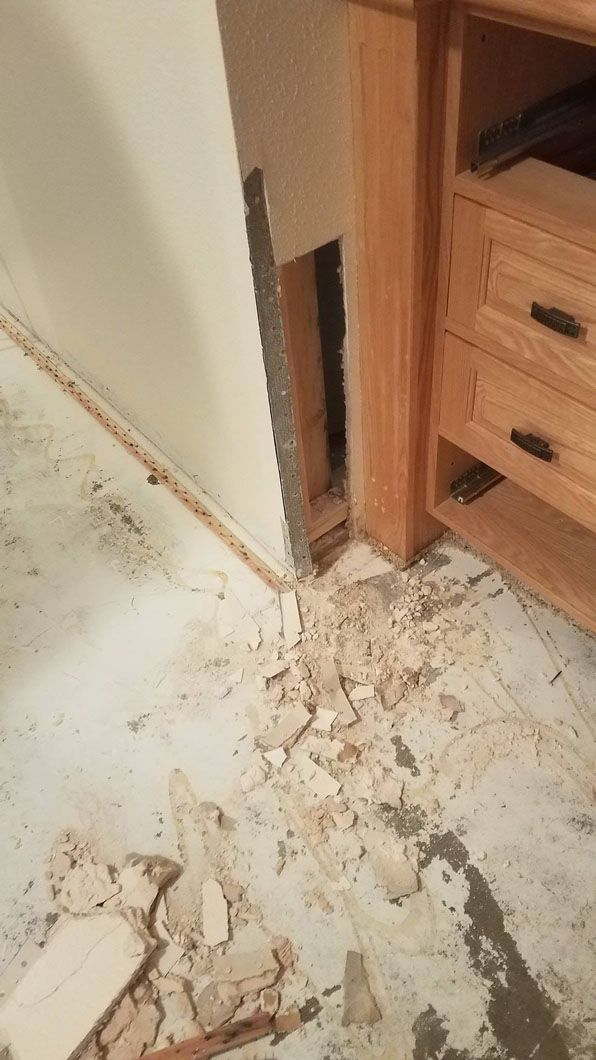 Damaged bathroom floor with broken drywall and debris beside a wooden vanity cabinet