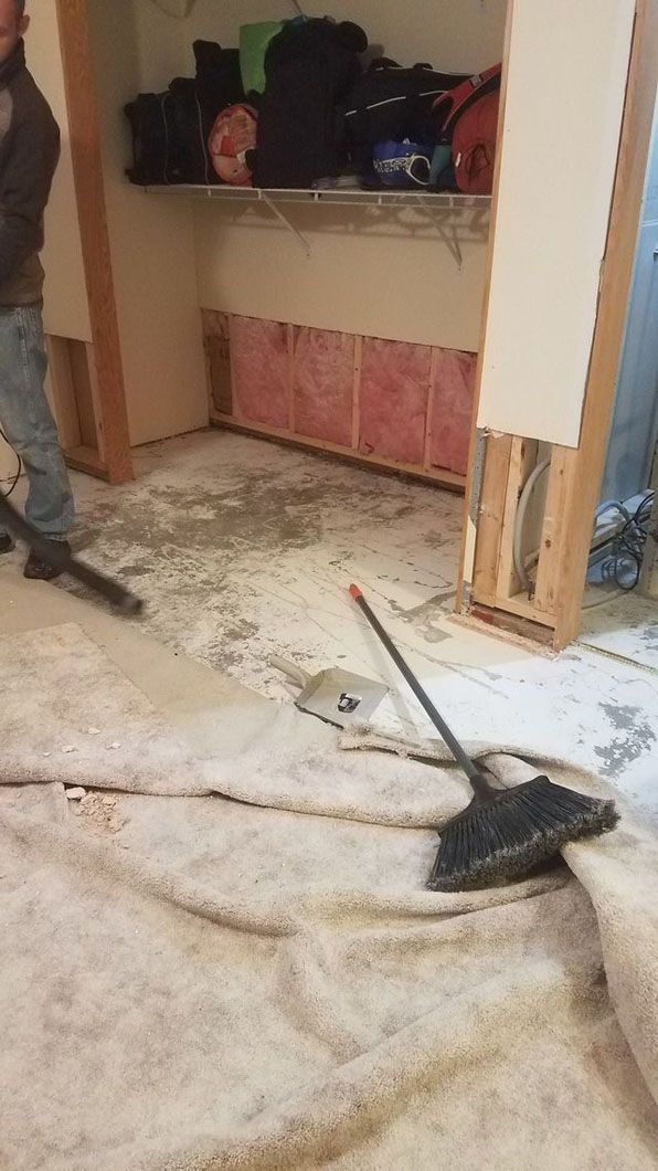 Partially demolished room with debris, a broom on the floor, and an open wall cabinet.
